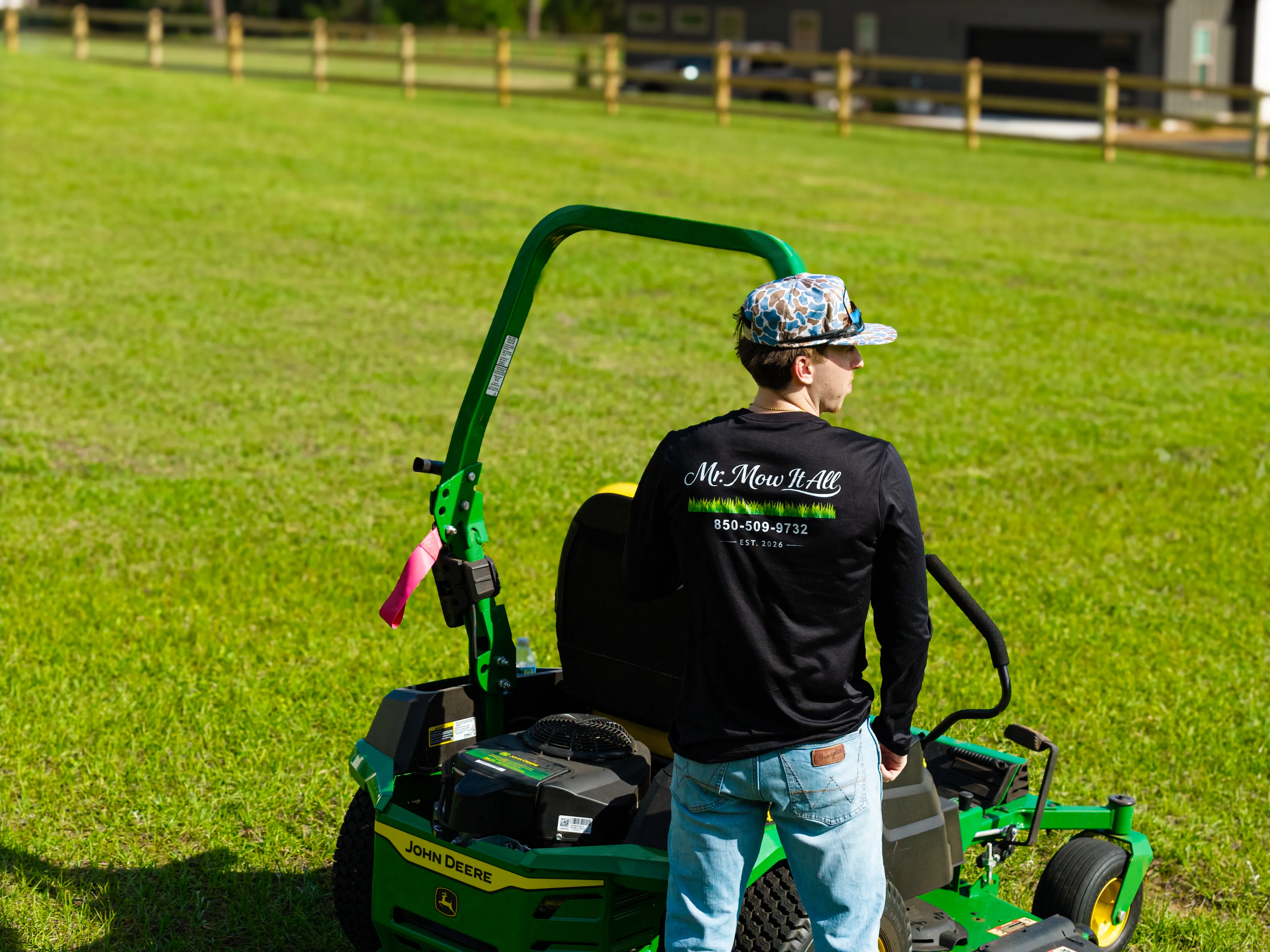 Mr. MowItAll operator in branded gear beside a green John Deere mower on a healthy lawn