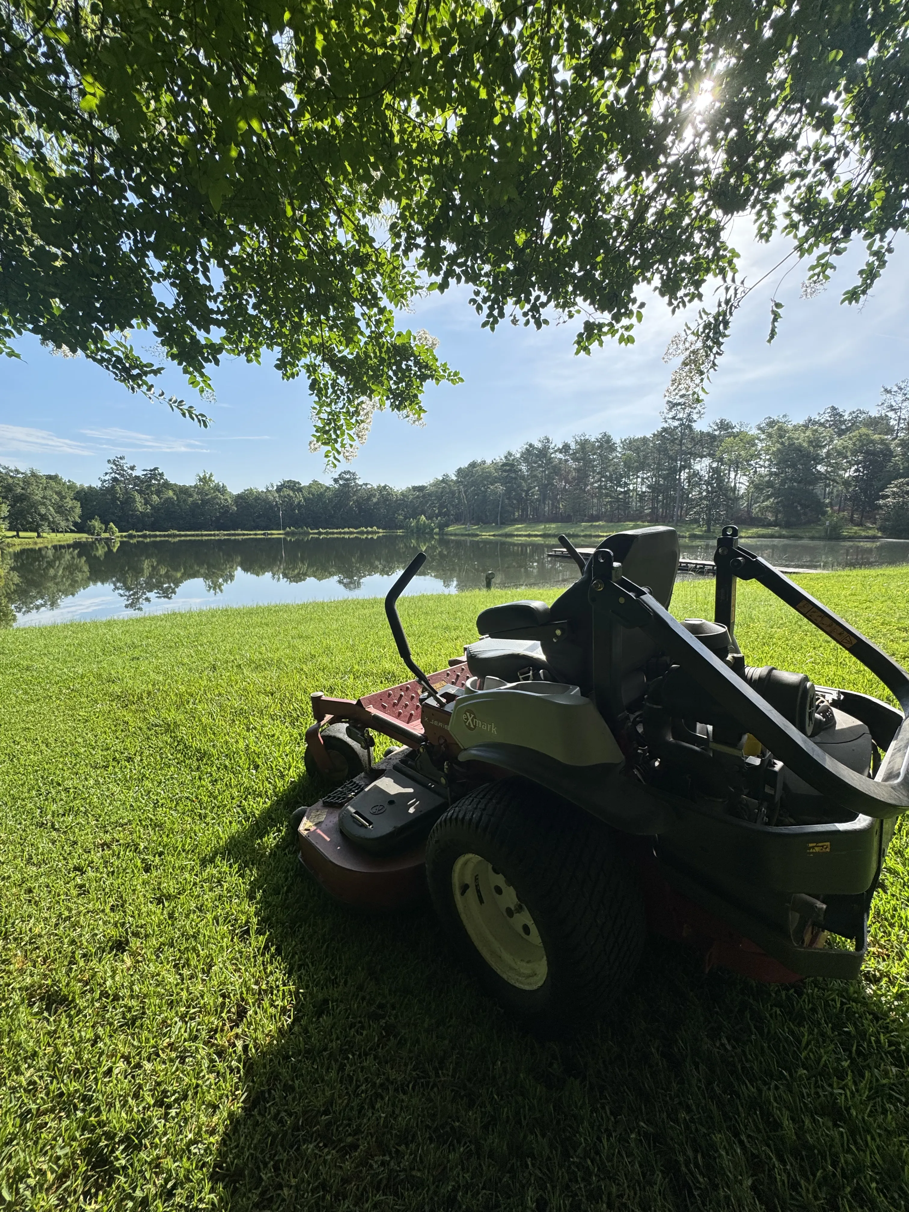 Mr. MowItAll zero-turn mower beside a calm pond on a freshly cut lakeside lawn