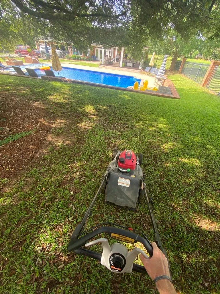Mr. MowItAll owner mowing a backyard lawn beside a swimming pool