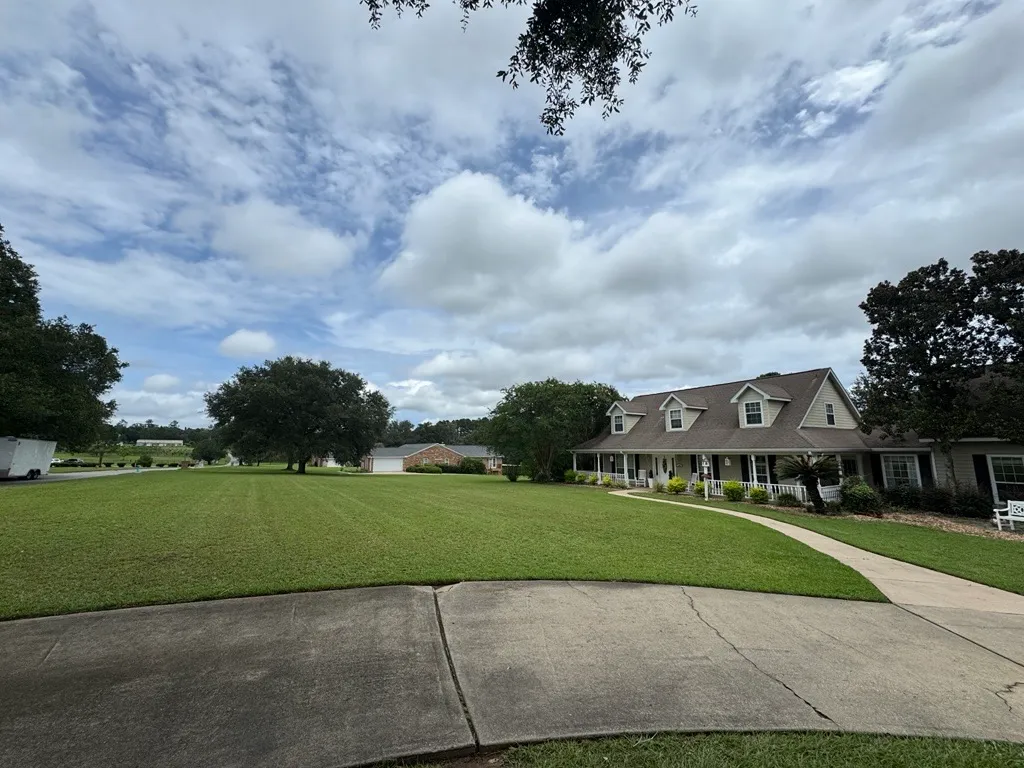 Wide, evenly cut front lawn sweeping up to a white two-story farmhouse with a covered porch
