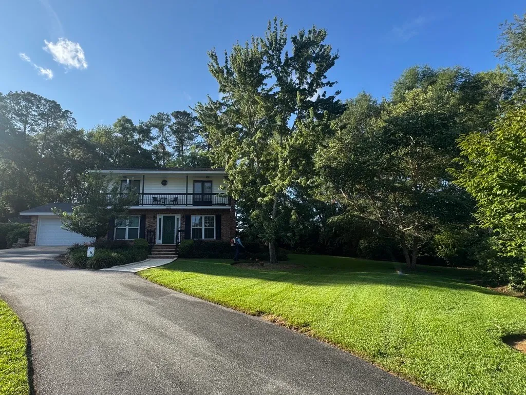 Freshly cut lawn along a curving driveway at a two-story home with a balcony porch, with a crew member clearing clippings