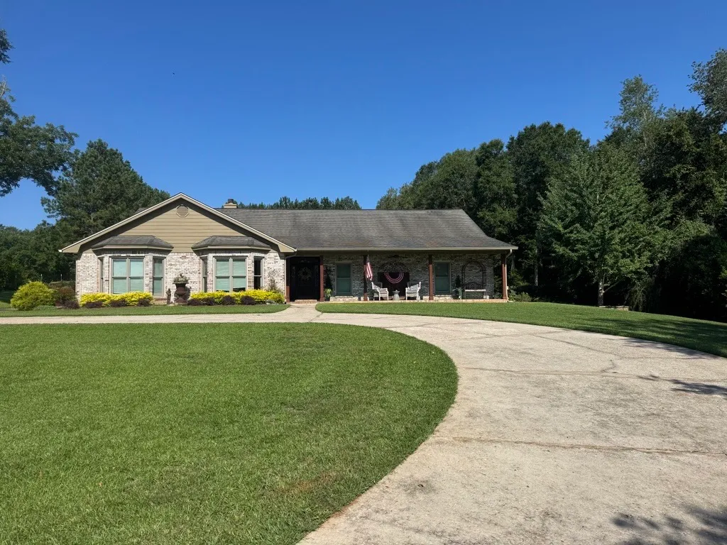 Crisp lawn edge along a circular driveway at a white brick ranch home with a flag and front porch
